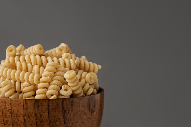 Gluten Free Cornmeal Pasta in wooden Bowl Spiral Raw Macaroni from Blend of Corn and Rice flour Close Up Front View Uncooked Bucati Pasta Food Background Horizontal banner with space for text