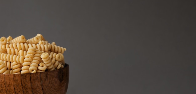 Glutenvrije maïsmeel pasta in houten kom spiraal rauwe macaroni van mengsel van maïs en rijstmeel close-up vooraanzicht ongekookte Bucati pasta voedsel achtergrond horizontale banner met ruimte voor tekst