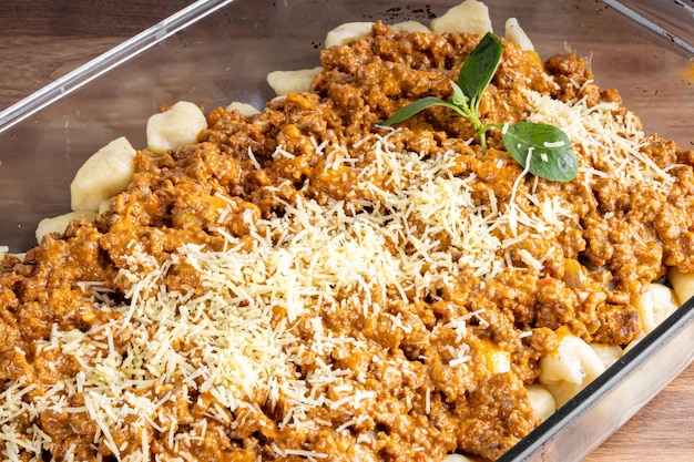 GNOCCHI COOKED WITH GROUND MEAT IN TOMATO SAUCE COVERED IN GRATED CHEESE MOUNTED ON A GLASS PLATTER