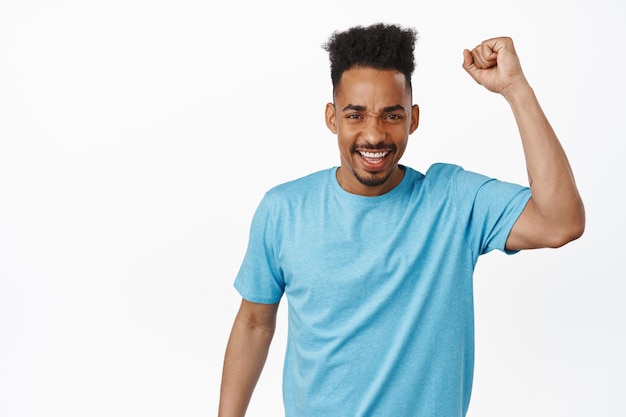 Go team. Excited activist, african american guy team fan, rooting, chanting and making fist pump gesture, smiling amazed, standing against white background.