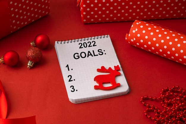 Goals for 2022 on a blank sheet of paper, among christmas gifts\
on a red background. concept of the upcoming christmas\
holidays