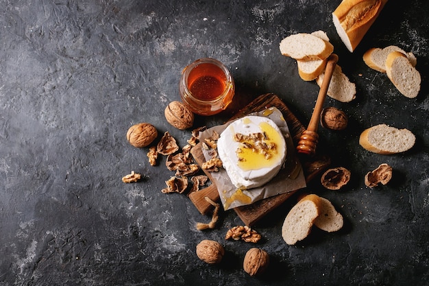 Goat cheese served with honey and walnuts over black texture background. Top view, flat lay. Copy space