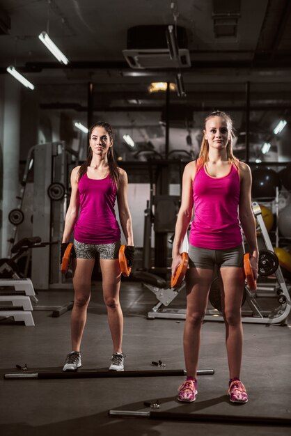 Goed gevormde vrouwen die waight platen in handen houden terwijl status in een gymnastiek.