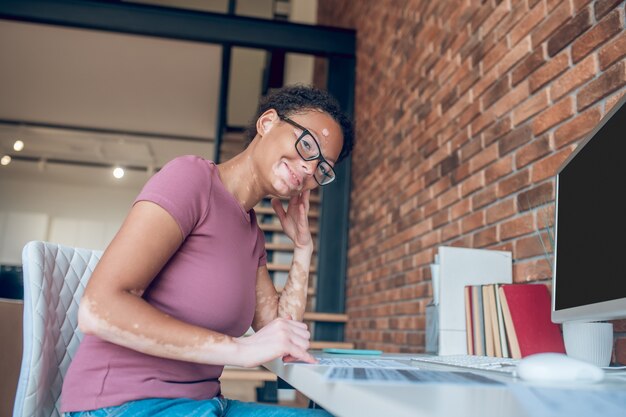 Goed gezind. Een vrouw met een bril die op een computer werkt en er gelukkig uitziet