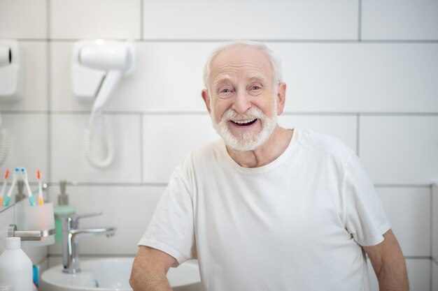 Goed gezind. Grijsharige man in witte t-shirt die krachtig lacht