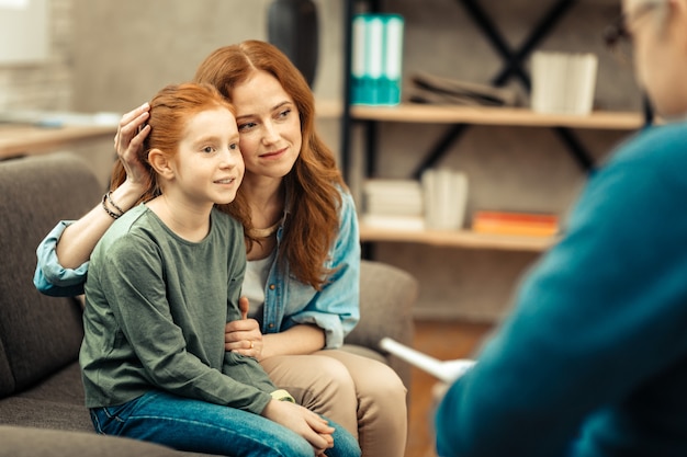 Goed humeur. Aardige jonge vrouw die lacht terwijl ze het haar van haar dochter aanraakt