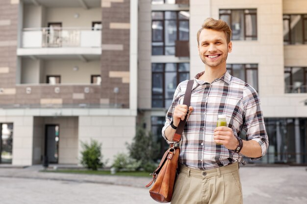 Goed humeur. Gelukkig vreugdevolle man die lacht terwijl hij een fles smoothie vasthoudt