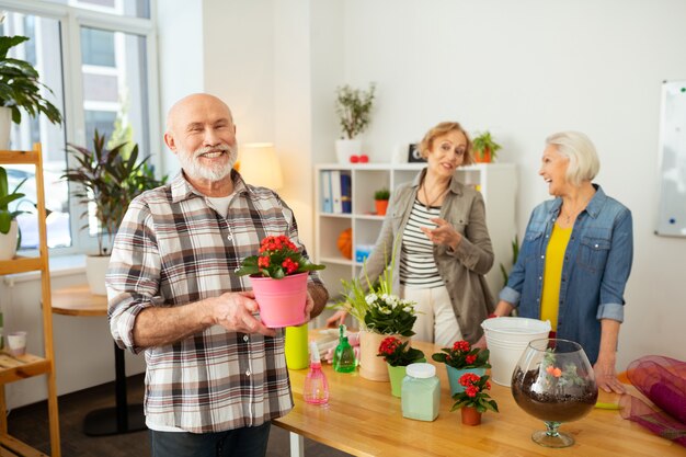 Goed humeur. Vrolijke senior man die naar je lacht terwijl hij een bloempot in zijn handen houdt