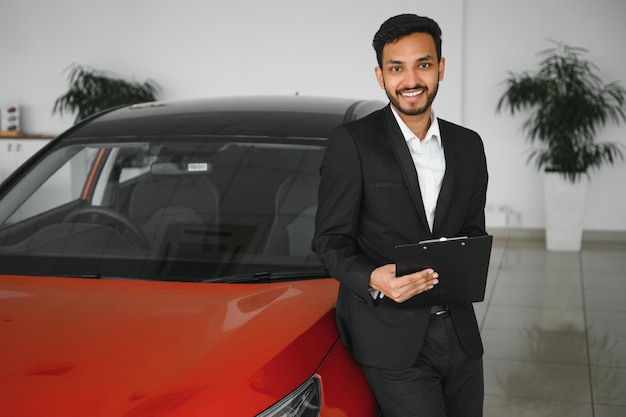 Goed uitziende, vrolijke en vriendelijke Indiase verkoper poseert in een autosalon of showroom