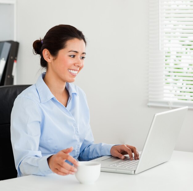 Goed uitziende vrouw ontspannen met haar laptop terwijl u geniet van een kopje koffie