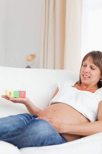 Goed uitziende zwangere vrouw spelen met houten blokken en het woord &quot;jongen&quot; geschreven op haar hand