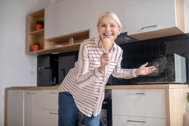 Goed voelen. Blonde huisvrouw met plezier in de keuken en lachend