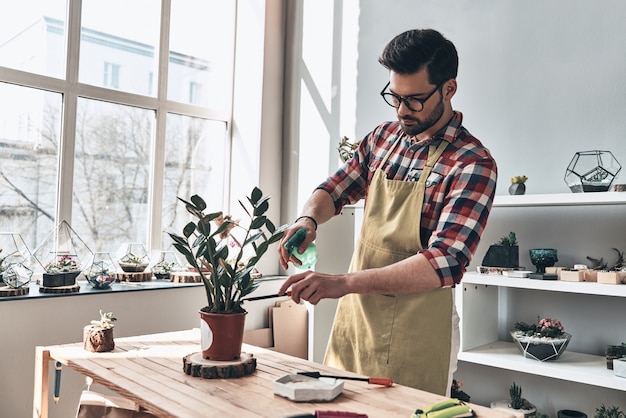 Goed voor planten zorgen. Knappe jonge man in schort die potplant water geeft