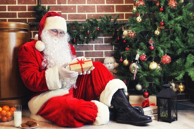 Goedaardige kerstman in een rood pak en witte baard bij de kerstboom