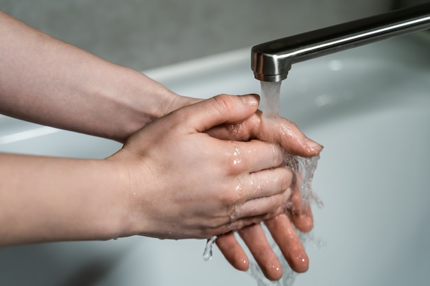 Goede hygiëne tijdens de pandemie van het coronavirus. Vrouw wast handen in warm stromend water met zeep