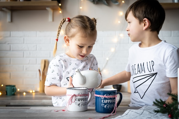 Goede kerstmorgen. Broer en zus drinken thee aan de keukentafel met koekjes in de keuken. Een tijd van wonderen en vervulling van verlangens. Vrolijk Kerstfeest.