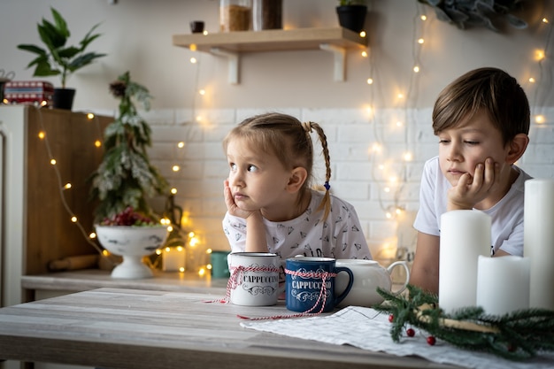 Goede kerstmorgen. Broer en zus drinken thee aan de keukentafel met koekjes in de keuken. Een tijd van wonderen en vervulling van verlangens. Vrolijk Kerstfeest.