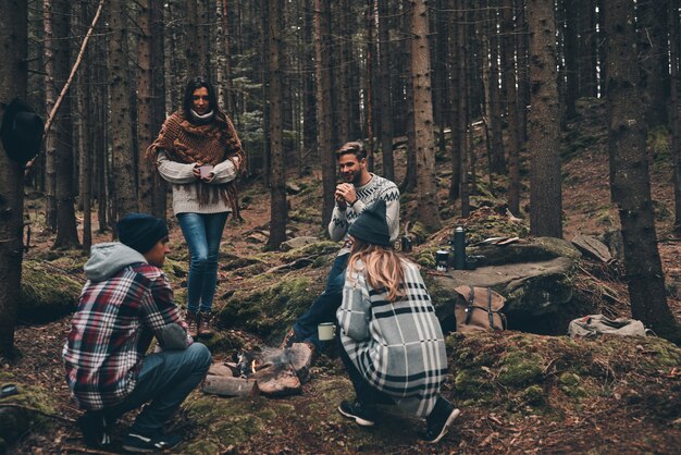 Goede vrienden. Groep gelukkige jonge mensen die rond het kampvuur staan tijdens het wandelen in het bos