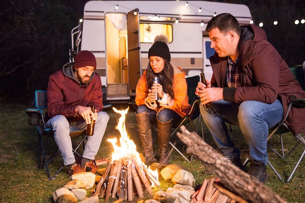 Goede vrienden zitten samen op campingstoelen rond het kampvuur in de bergen. Retro camper.