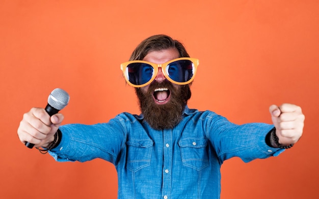 Goededag. man zingt muziek in de microfoon. grappige bebaarde man met microfoon. brutale blanke hipster in feestbril. karaoke zanger. ongeschoren man met verzorgd lang haar.