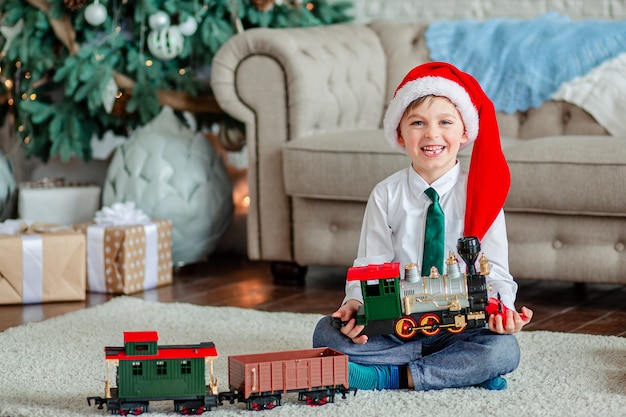 Goedemorgen. Gelukkig jongetje met een geschenk, speelgoed trein, onder de kerstboom. Tijd om wensen te vervullen.
