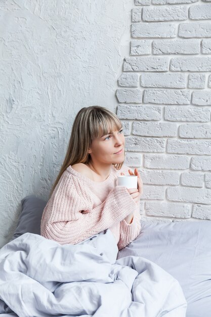 Goedemorgen met koffie. Jonge vrouw in bed met kop