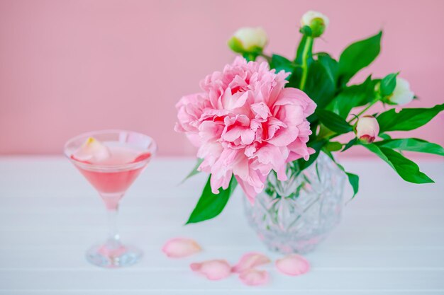 Goedemorgen. Roze pioenrozen in een kristallen vaas op een roze houten achtergrond, kopieer ruimte, close-up.