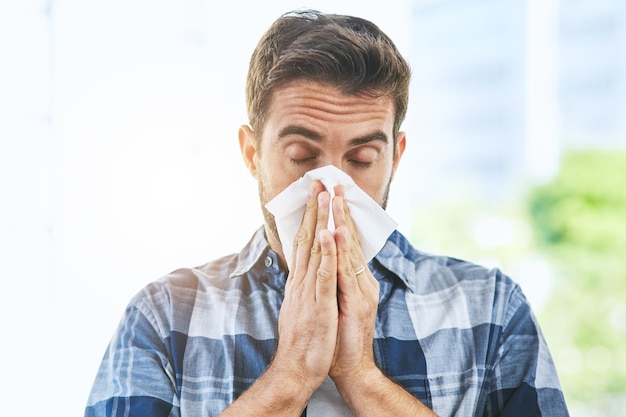 Going t have to stock up on tissues Portrait of an uncomfortable looking young man blowing his nose with a tissue inside of a building during the day