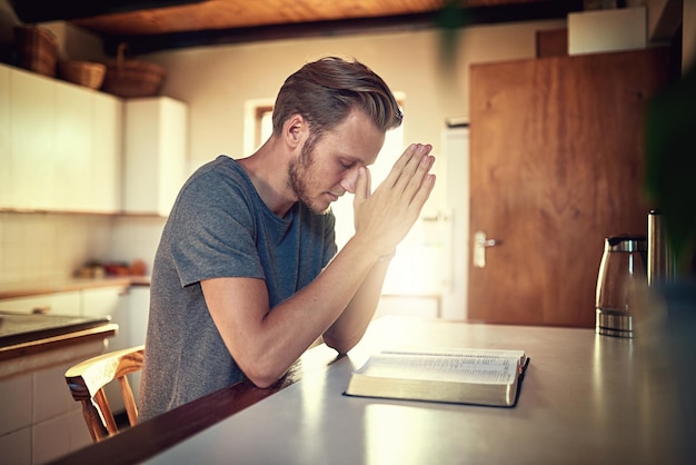 Going through his daily devotions Shot of a devoted young man clasping his hands in prayer over an open Bible