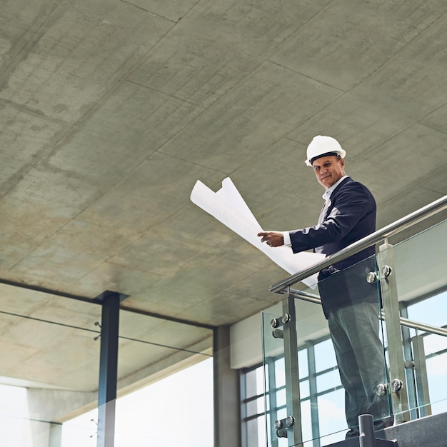 Going through the plans like the boss he is Portrait of a cheerful professional male architect looking at the camera while holding blueprints inside a building