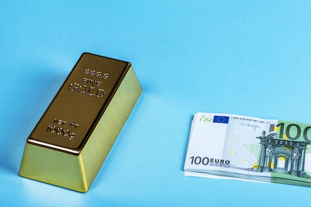 Золотой слиток, слиток, слиток и банкноты евро в денежном пакете на синем фоне.