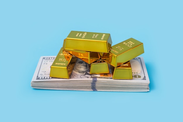 Gold bars and dollars on a blue table.