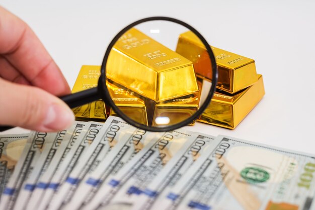 Photo gold bars on dollars with a magnifying glass. a hand with a magnifying glass checks the gold bar.