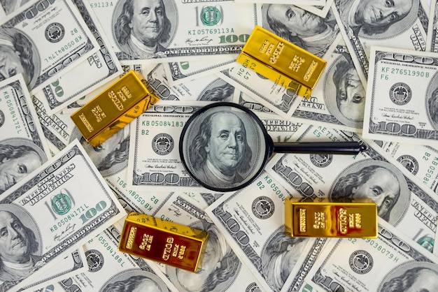 gold bars with a magnifying glass on dollars Financial saving concept gold and dollars