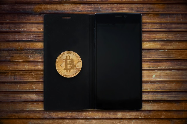 Gold bitcoin cryptocurrency with a smartphone on a wooden table Electronic money mining concept copy space