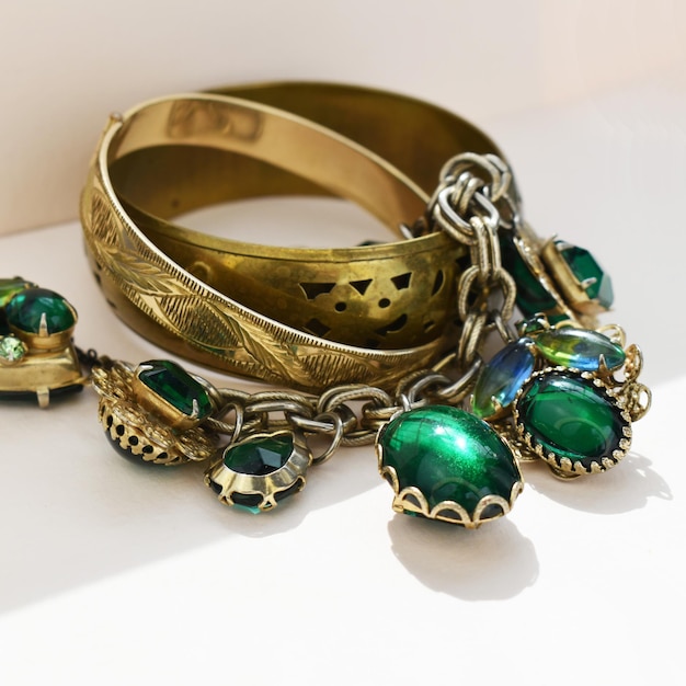 gold bracelet with green emeralds and chains on a white background