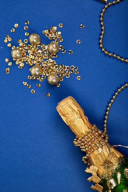 Gold champagne bottle with golden confetti on blue paper background