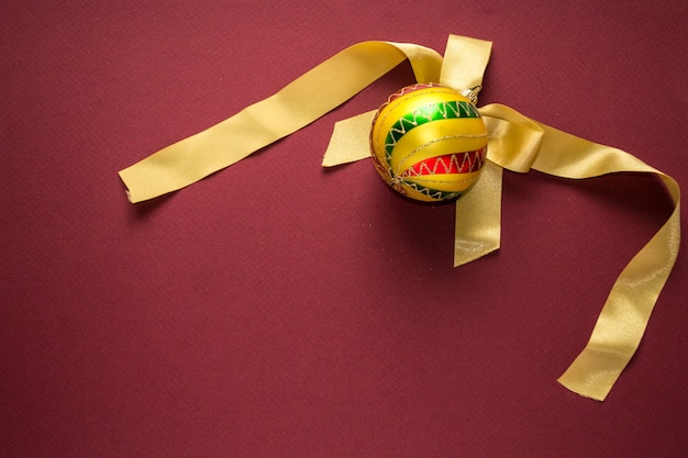 Gold christmas new year ball decoration with colorful stripes with from tree on bordo back