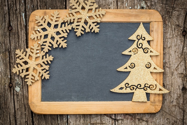 Gold Christmas tree decorations on vintage wooden blackboard with copy space. Xmas holidays card