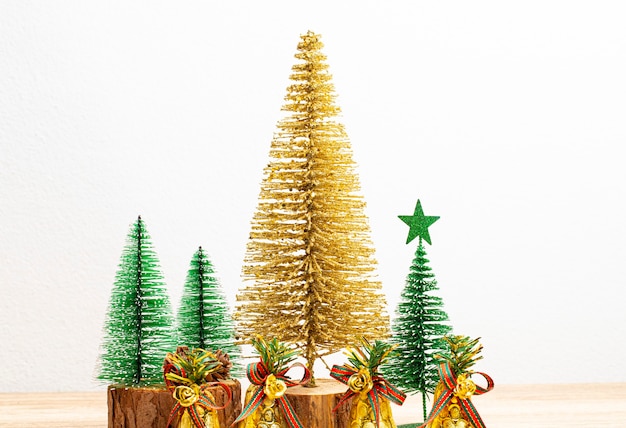 Alberi di natale d'oro e alberi di natale verdi con campane d'oro sul tavolo e sfondo bianco. vista frontale, copia dello spazio.