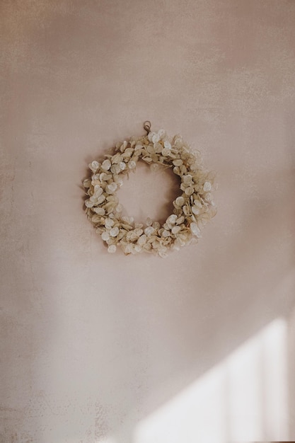 Gold Christmas wreath made of natural dry lunaria leaves hanging on a pink wall with sunlight shadows New Year and winter holidays Aesthetic Christmas decor