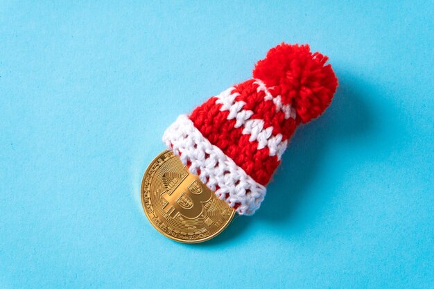 青い背景にクリスマスキャップが付いたビットコインサイン付きの金貨暗号通貨マイニング