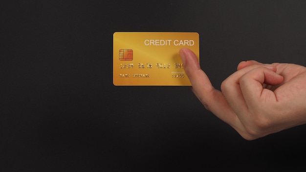 Gold color credit card in hand on black background.