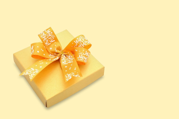 A gold color present box with a bright yellow ribbon on yellow background