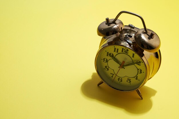 Gold colored alarm clock on yellow background