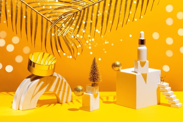 Gold composition with cream and serum, geometric shapes and Christmas tree, on a yellow wall with palm leaves, concept of beauty and cosmetics.