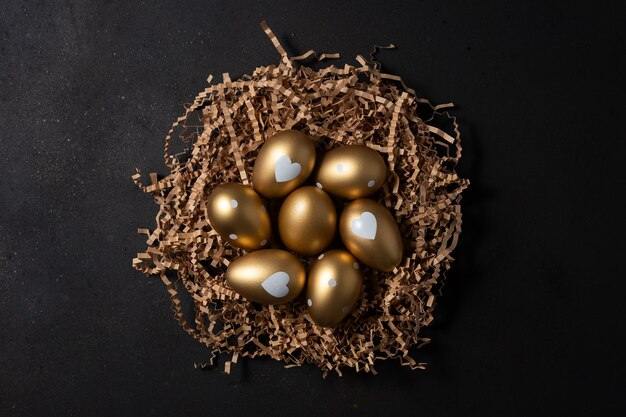 Gold eggs in paper nest on black background Top view