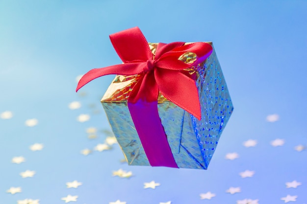 Золотая подарочная коробка с красной лентой, плавающей на синем фоне с блестящими звездами