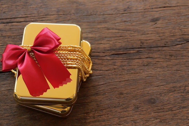 Gold gift boxes with gold necklace and ribbon on brown wooden background