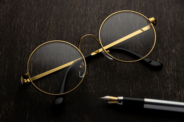 Gold glasses, pen on a dark wooden background..